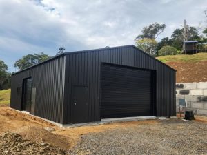 Black colorbond shed with two roller doors and personal access doors